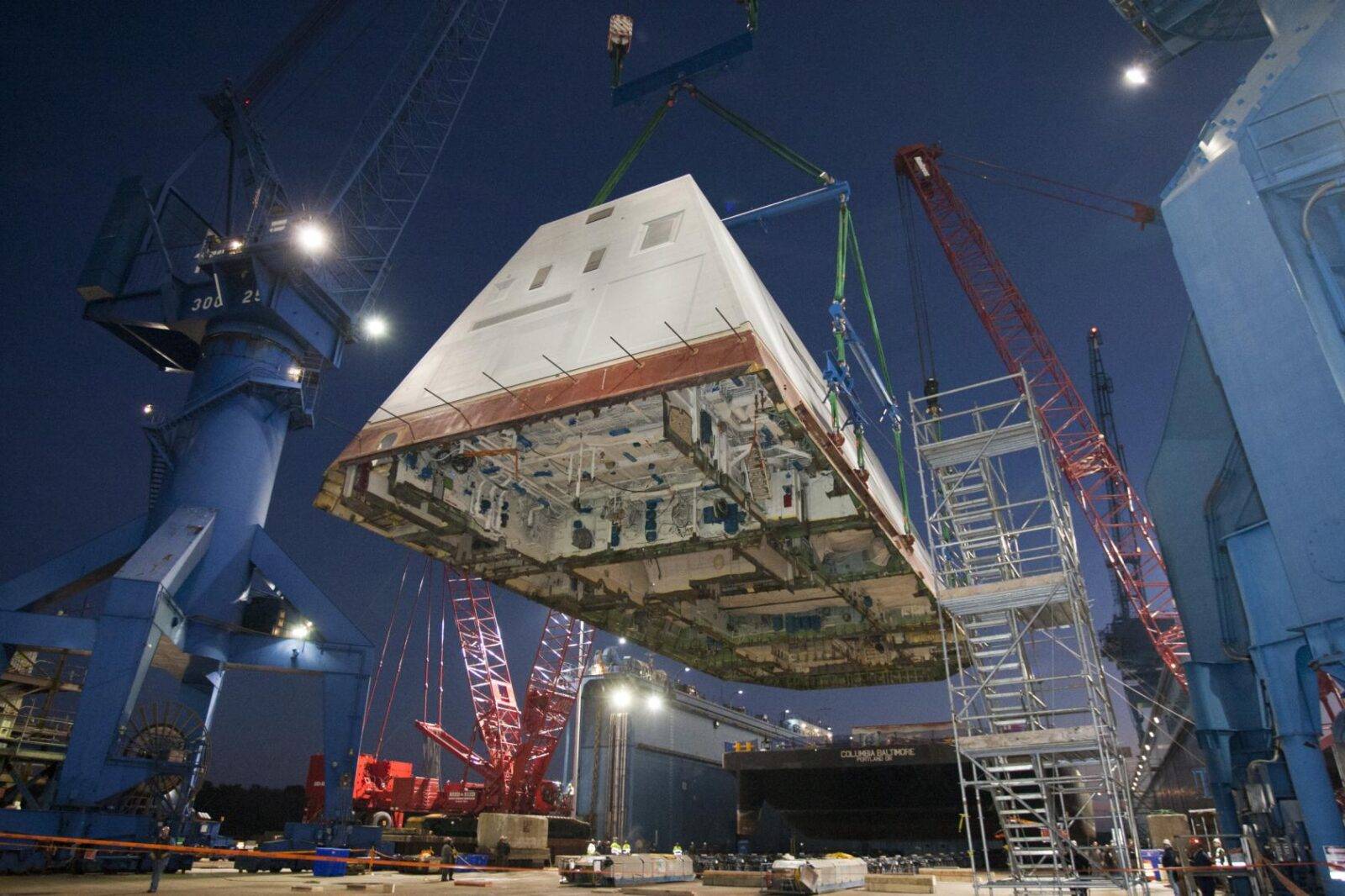 (2012) The 1,000 ton deckhouse of a future destroyer is craned toward the deck of the ship to be integrated with the ship’s hull at General Dynamics Bath Iron Works. Photo by: U.S. Navy